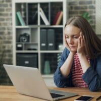 Event Planner Sitting At Computer Concerned About Avoiding Speaker Cancellations